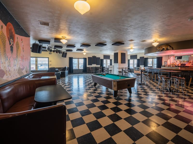 Empty upstairs room with checkerboard floor, pool table, stage gear and bar
